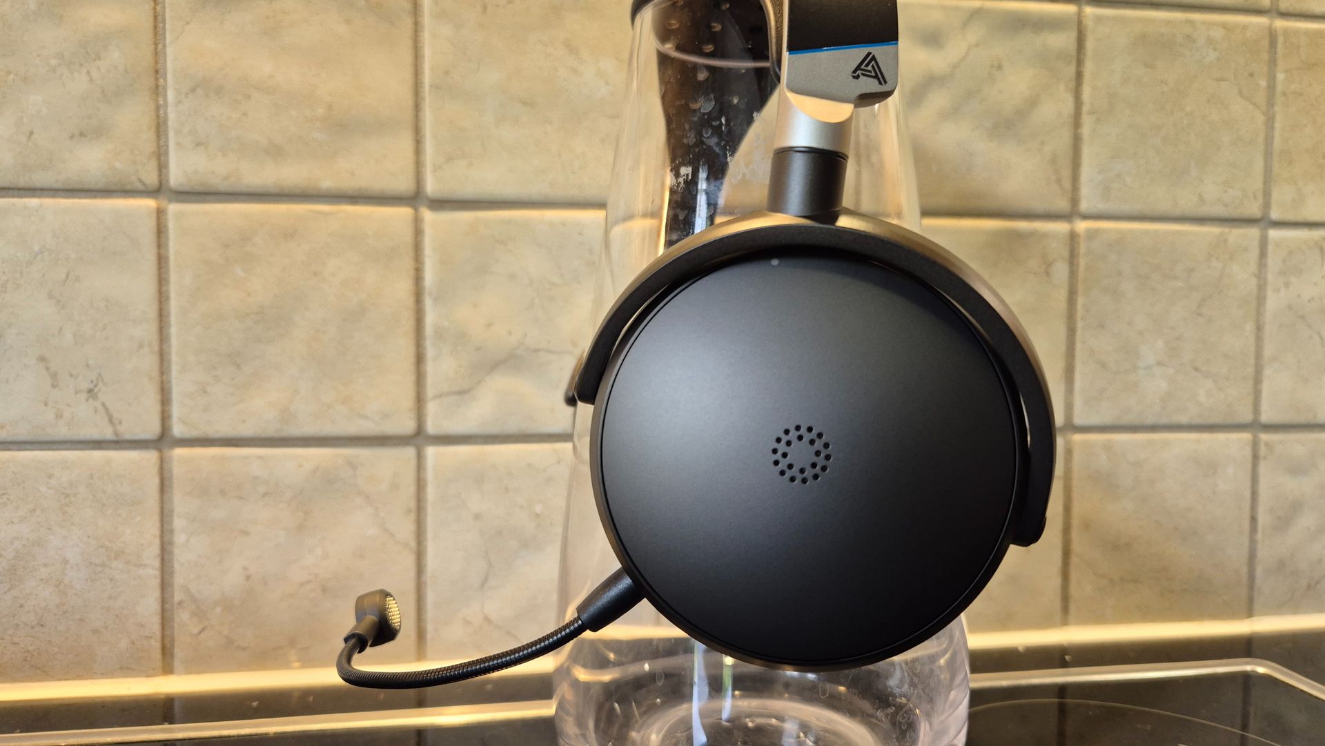 A picture of the Audeze Maxwell 2 ANC gaming headset clamped around a glass vase with pale tiles in the background