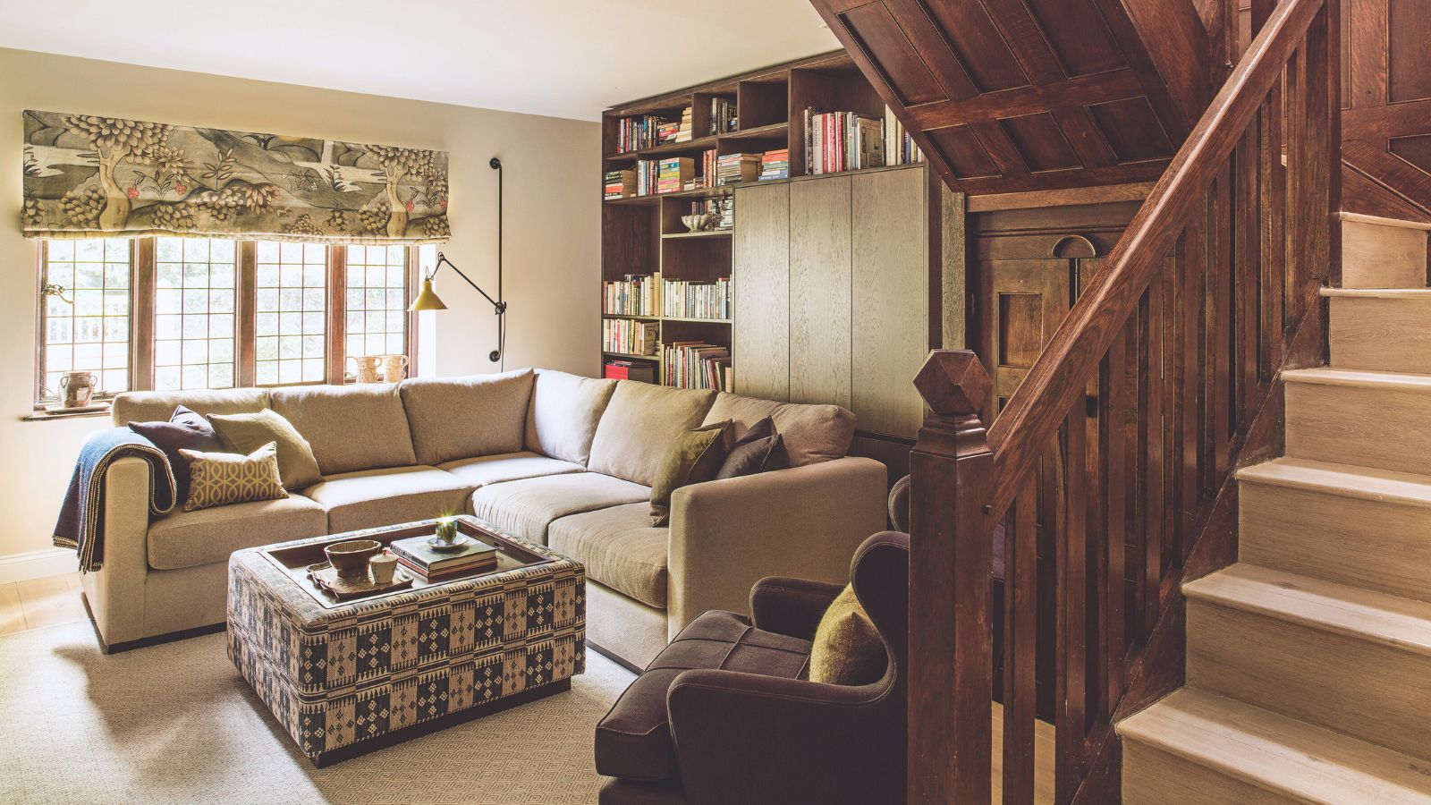 A landing area with a staircase and wooden banister, and a seating area with a large sofa and footstool. Fitted bookcases. 