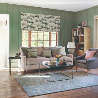 A living room with green-coloured wall panelling and a beige sofa with scatter cushions matching the panelling