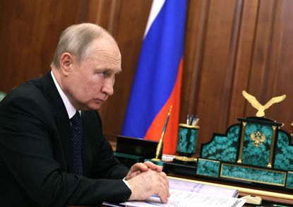 Russian President Vladimir Putin sits at a table with his hands crossed