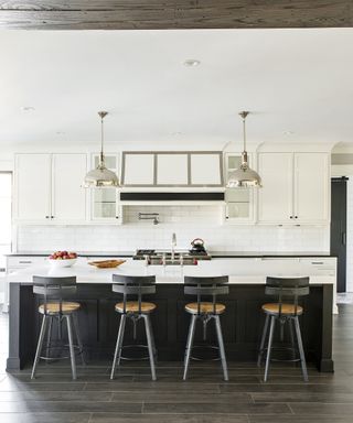 A white kitchen with a black island and wooden bar stools