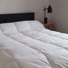 A duvet on a bed with a black headboard in a bedroom with a black bedside lamp