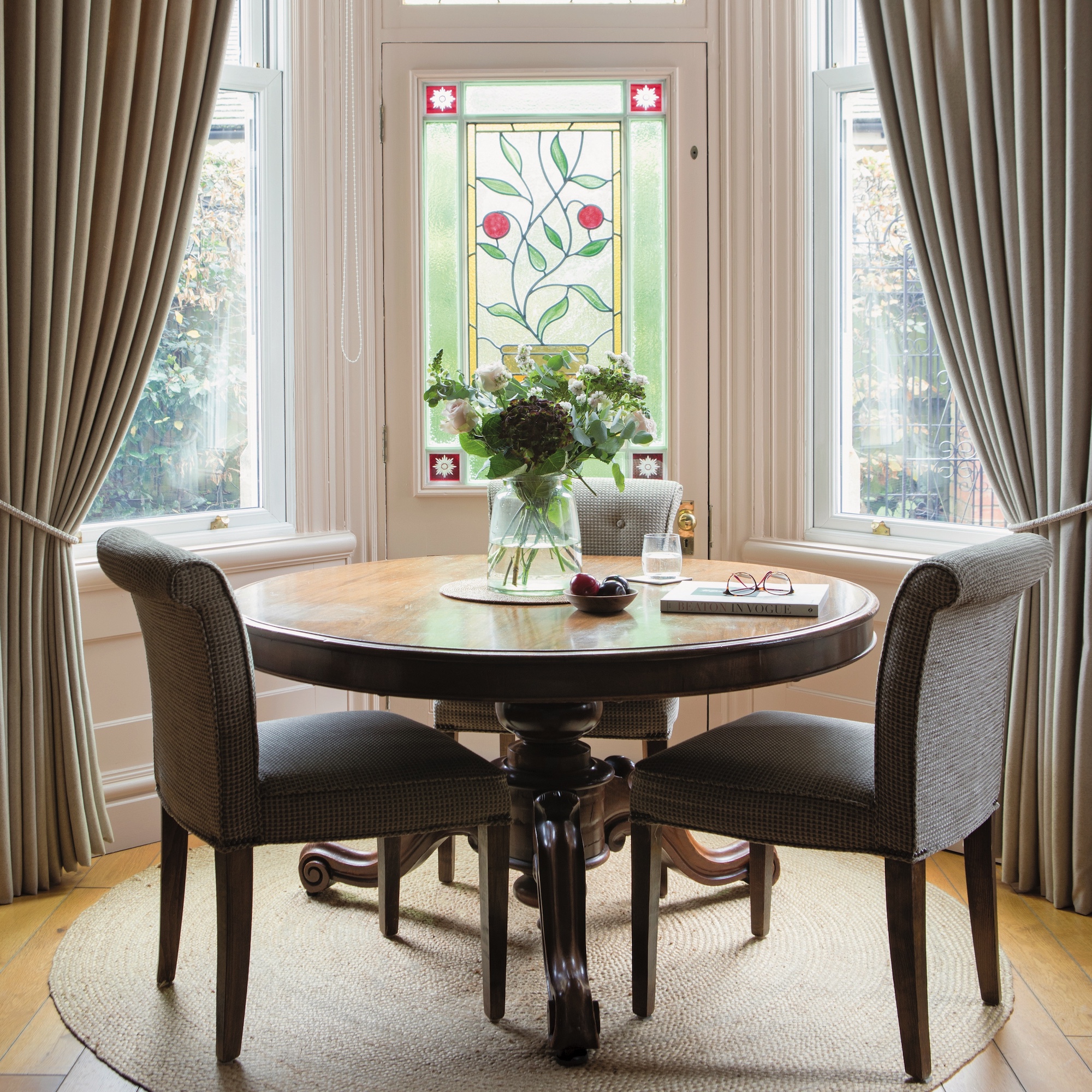 sitting room with large bay window with stained glass and circular table with upholstered dining chairs in front