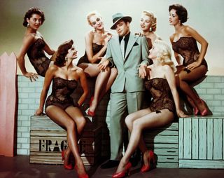 marlon brando in a grey suit with women in leotards around him in Guys and dolls