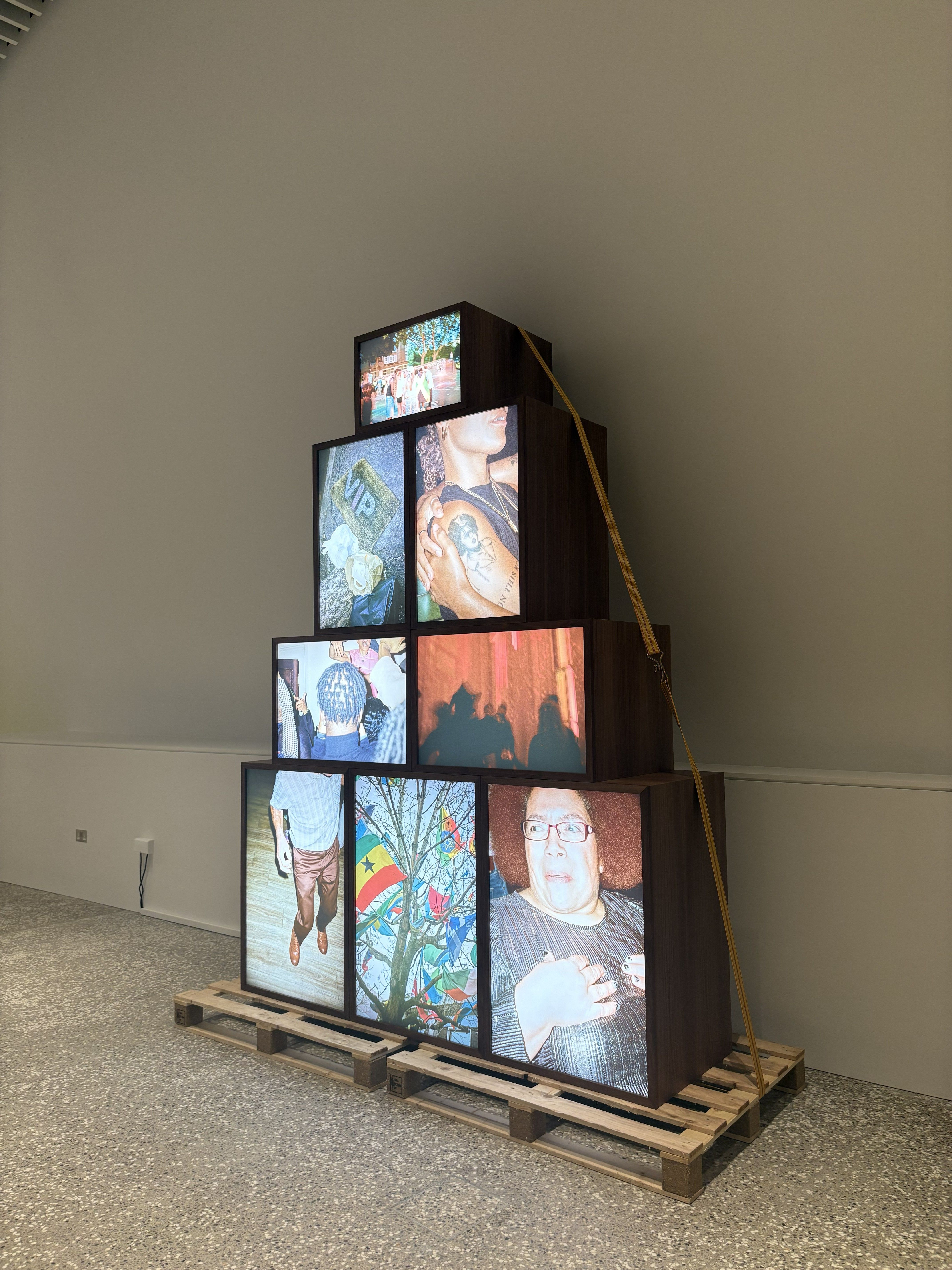 The interior of a museum, featuring a curated book shelf and a towering, pyramidal installation of multiple screens placed atop each other.