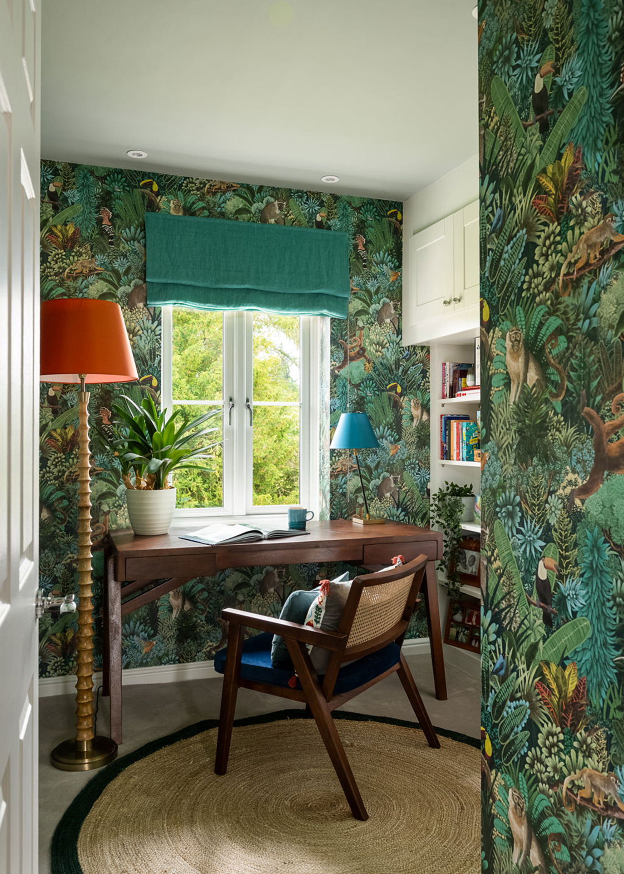 home office with jungle patterned wallpaper and a desk beside a window