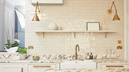An off white kitchen with gloss metro wall tiles above a marble worktop and brass wall lights either side of an open shelf 