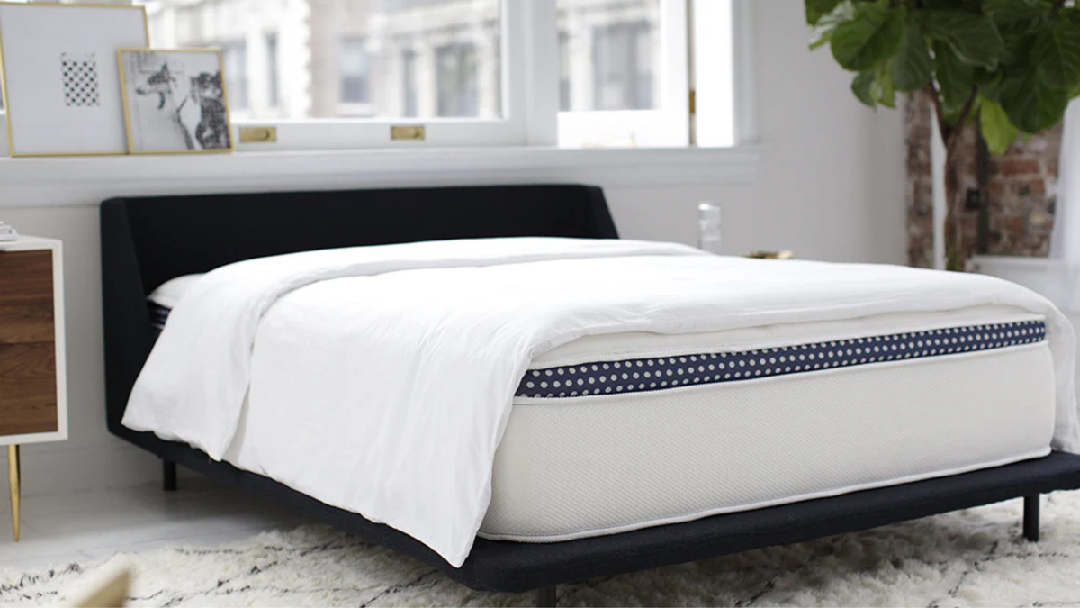 The WinkBeds Plus mattress on a bed frame with a duvet in a brightly lit room