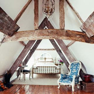 attic bedroom with wooden floorboard and wooden beam and white wall and armchair