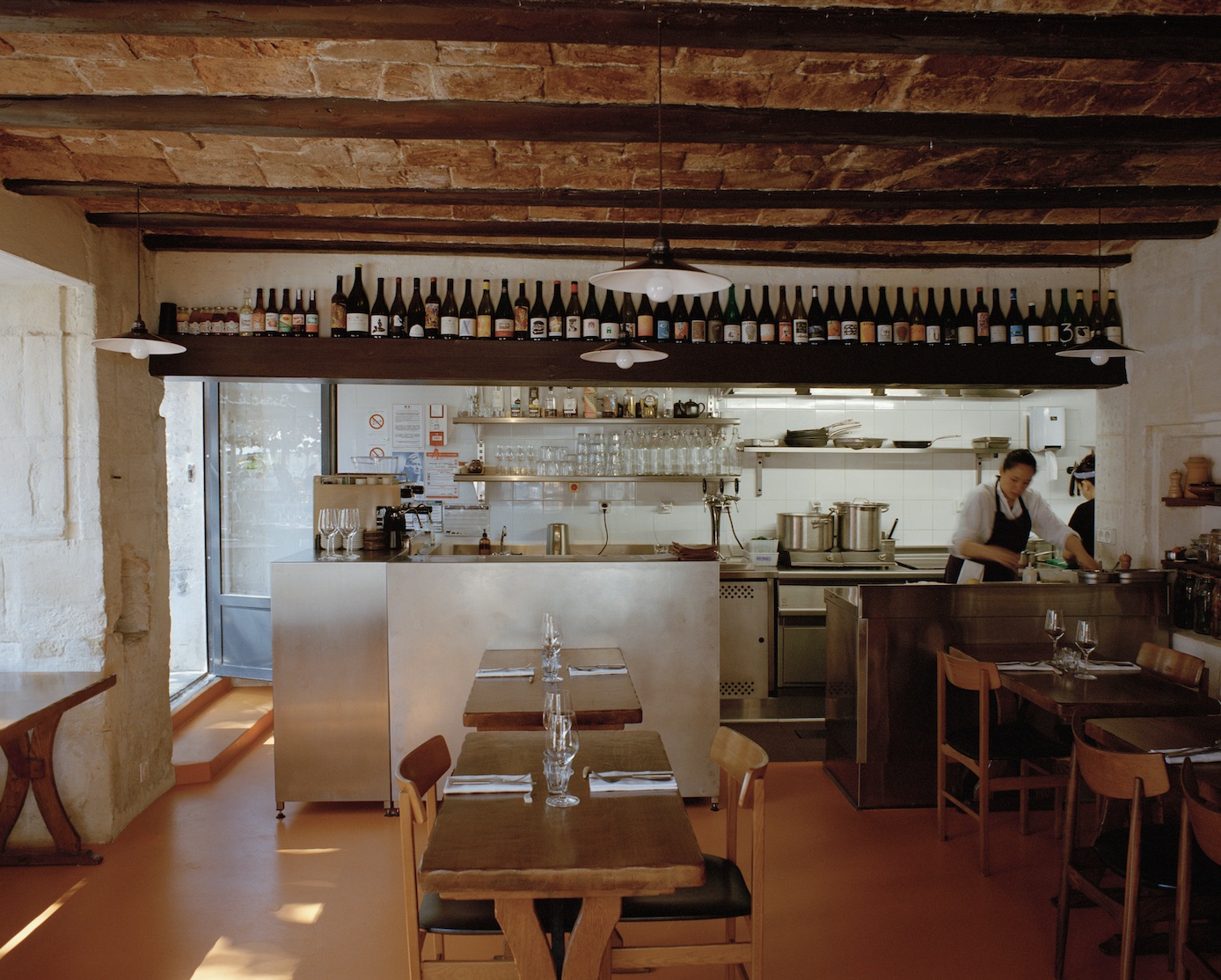 A sun-filled, intimate restaurant pairs stone ceilings with exposed beams and historical walls with chrome accents and bistro-style dining tables in wood.