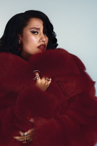 singer raye poses while wrapping herself in a red faux fur coat