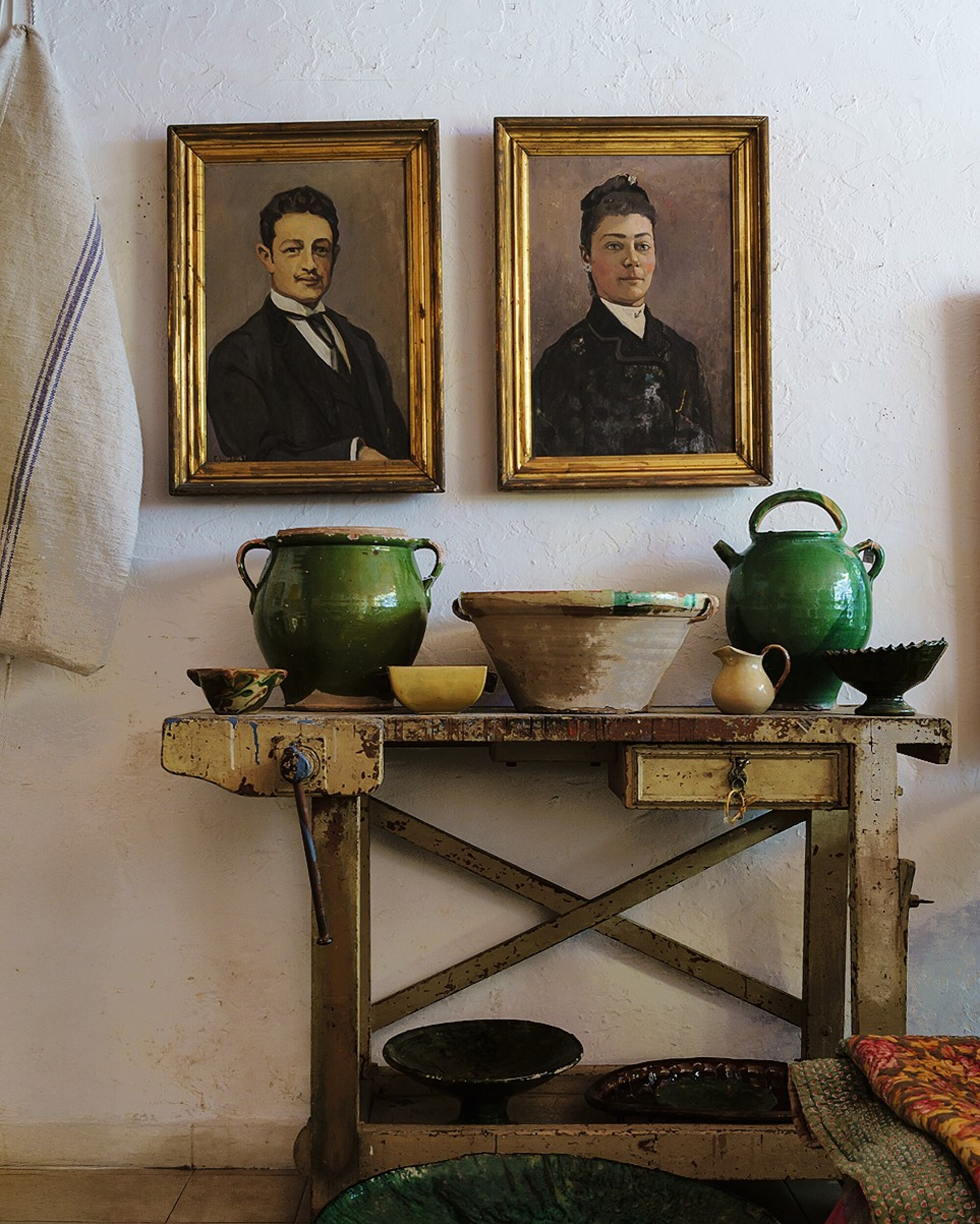 antique table with green ceramics, bowls, two antique oil paintings with gold frames on the wall