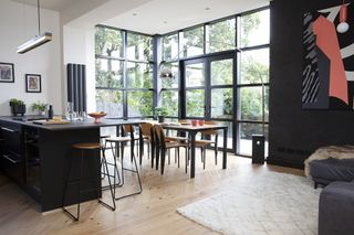 Open-plan kitchen-diner with black kitchen units, glazed aluminium wall and doors out to garden, black and wood dining set