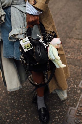 a woman at London fashion week carries a multicolor beanie baby attached to her purse