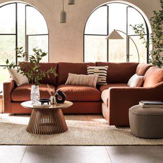 A living room with large arched windows and a corner sofa in a rusty red