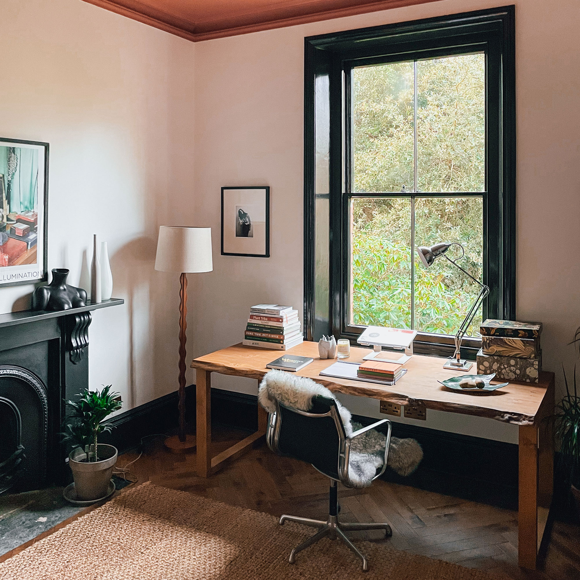 Neutral home office with large black-framed window, wooden desk, woven rug and black fireplace