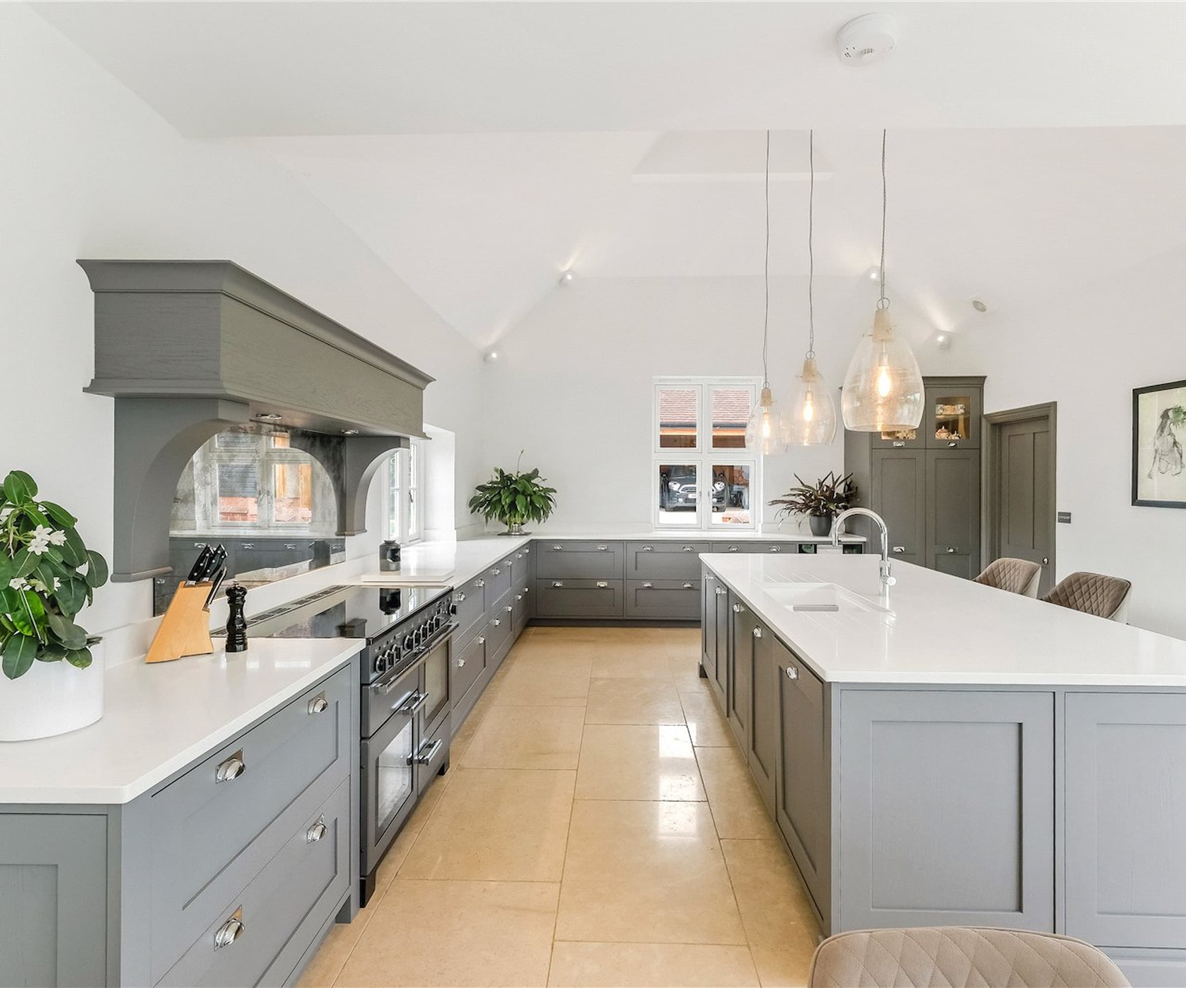 A kitchen with grey cabinets and a kitchen island with white surfaces with ceramic flooring