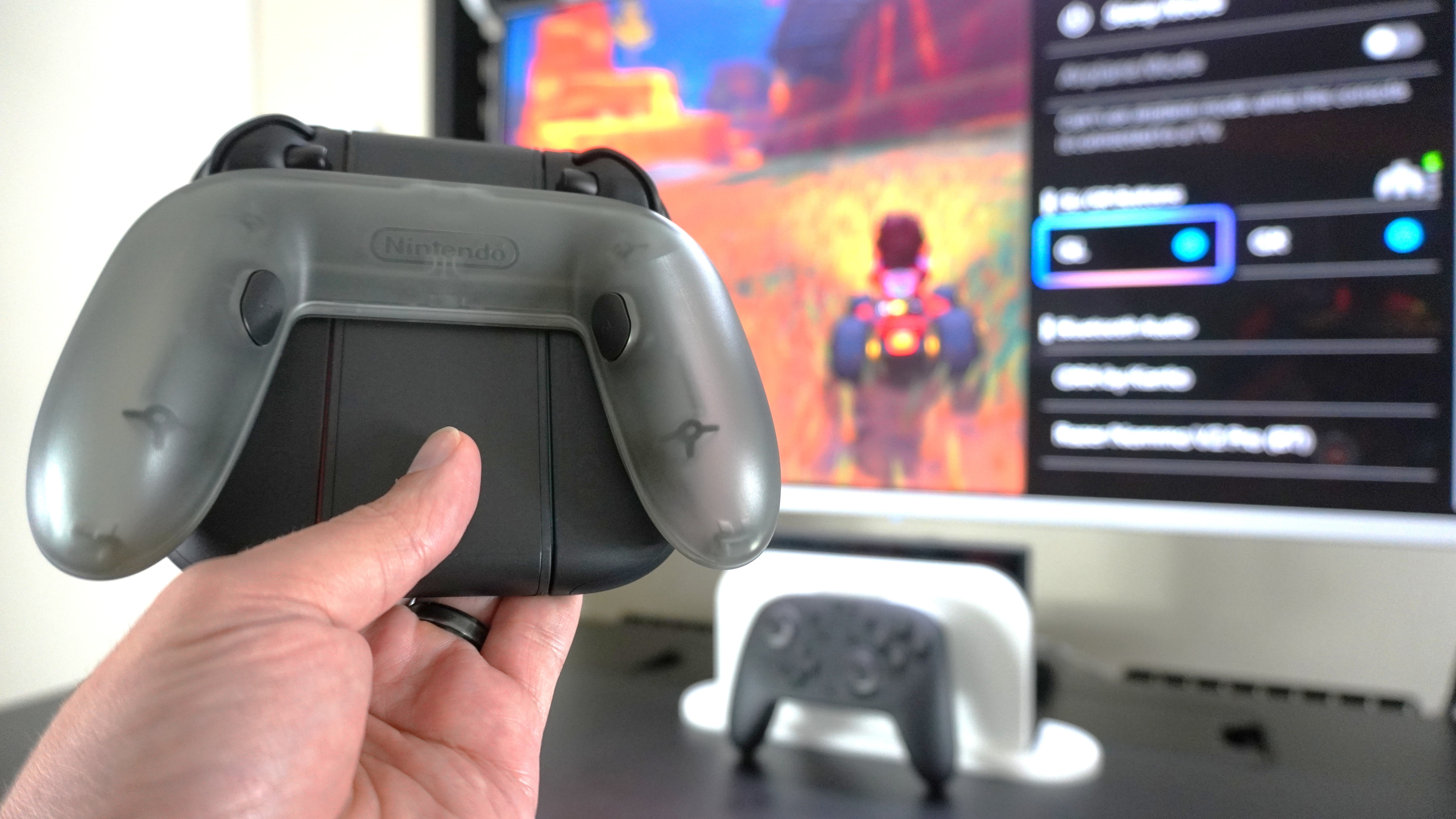 A person holding up the Joy-Con 2 Charging Grip in front of a Switch 2 with the console's Quick Settings menu visible on screen showing how you remap the controller's GL/GR buttons