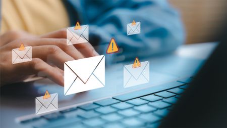 A person types on a laptop keyboard with envelope and warning icons hovering above, indicating email security threats