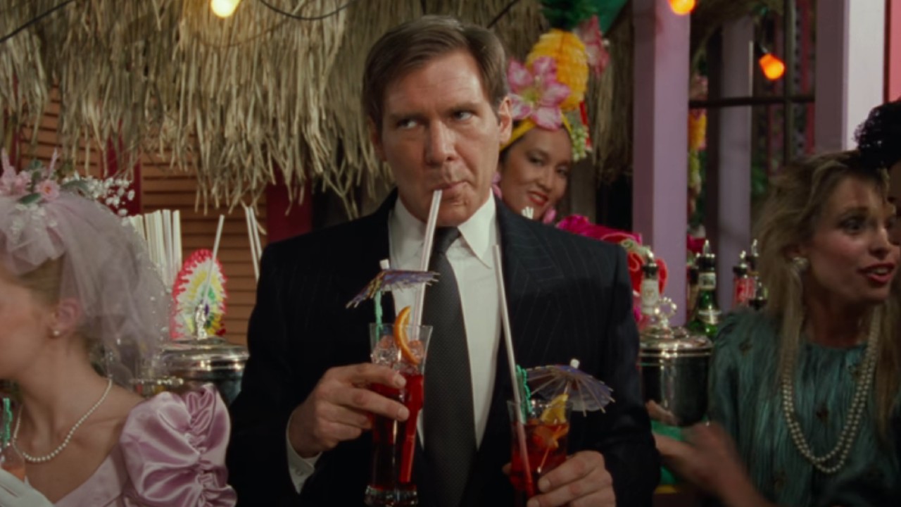 Harrison Ford drinking a tropical drink and holding another one in the other hand.