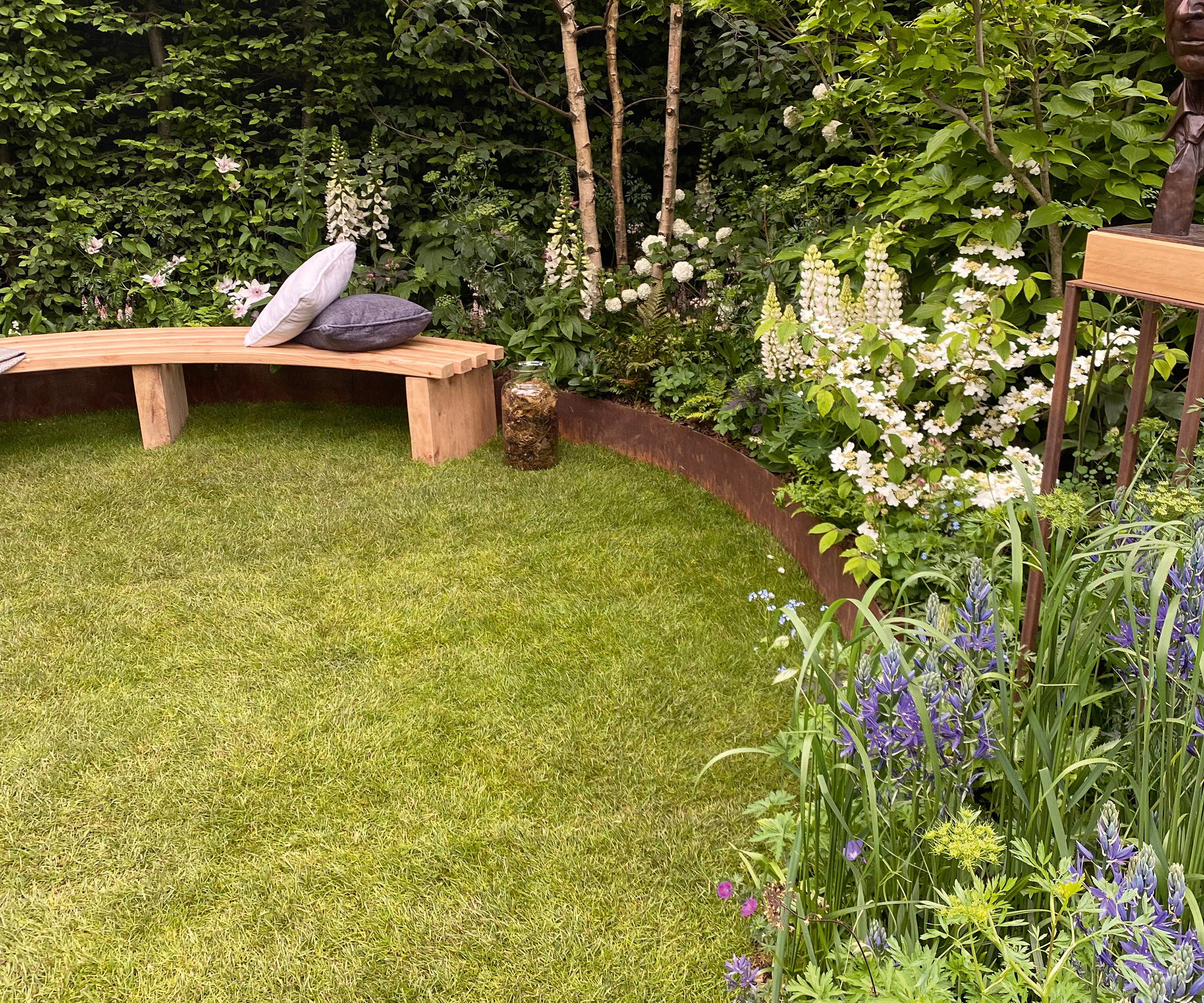 A curved lawn with metal garden edging framing a flower bed with a wooden bench