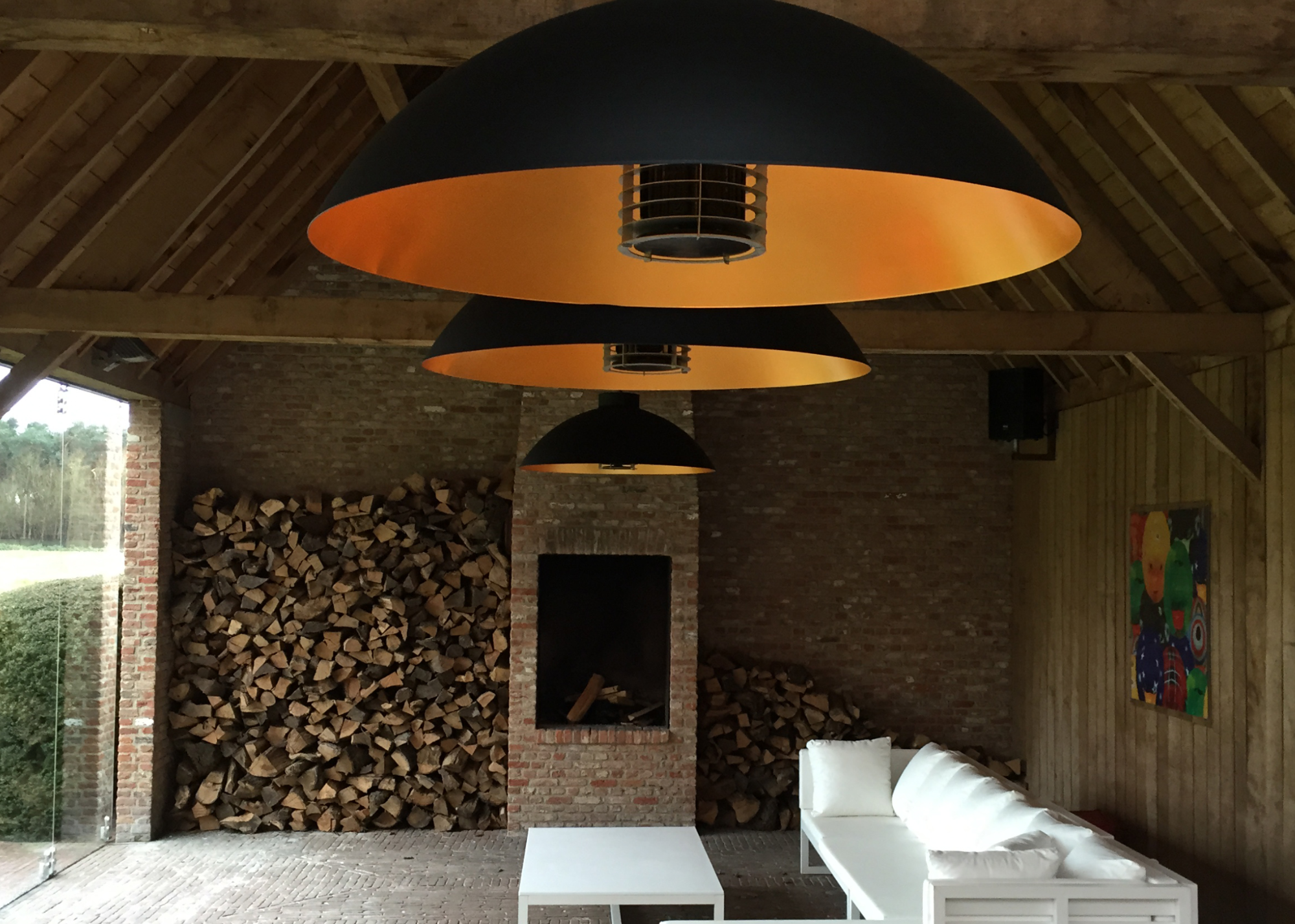 Overhanging patio heater in open barn with a large sofa on one side of the room and a table in the middle