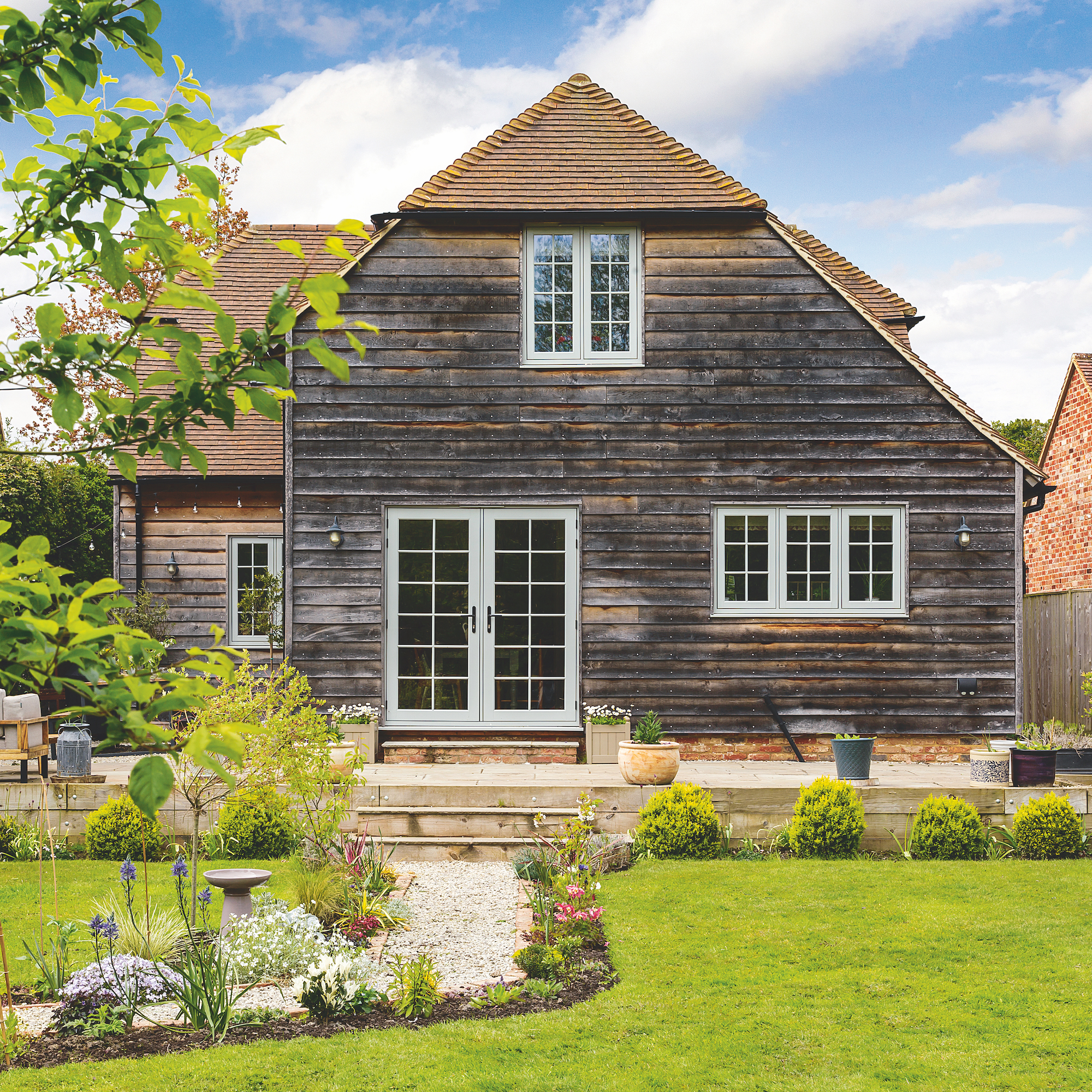 exterior of wood clad new build cottage with patio doors on to garden and lawn