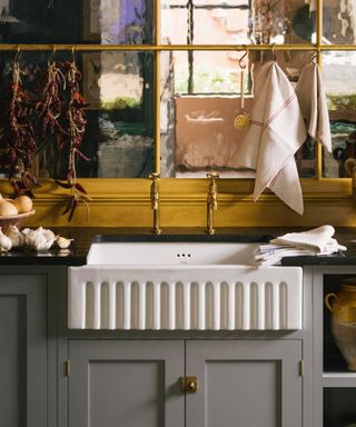 Fluted sink with gray cabinets, mirror behind, brass hanging rail,