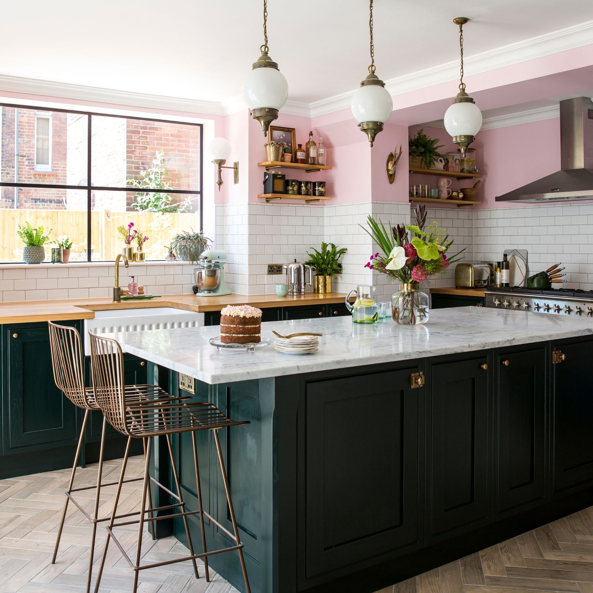 Dark green kitchen units with marble style worktops, open shelves and metro tiles with pink walls