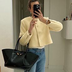 Woman wearing black Demellier London New York work tote with cropped, button-down jacket and blue jeans standing in front of mirror