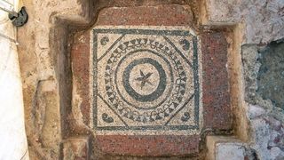 A picture of the mosaic discovered at the center of the mausoleum features a flower and concentric circles.