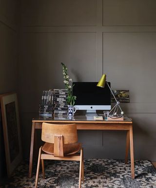 gray-brown wall with wooden desk and chair with computer and green lamp