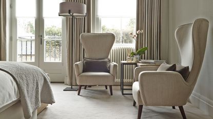All cream bedroom with carpeted floors, large windows, armchairs and Juliette doors that open onto balcony