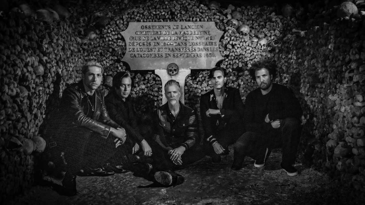 Queen Of The Stone Age crouched in a catacomb, surrounded by skulls