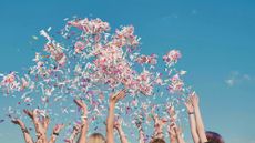 Group of students throwing colorful confetti in the air on a sunny day
