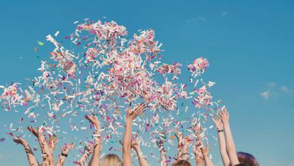 Group of students throwing colorful confetti in the air on a sunny day