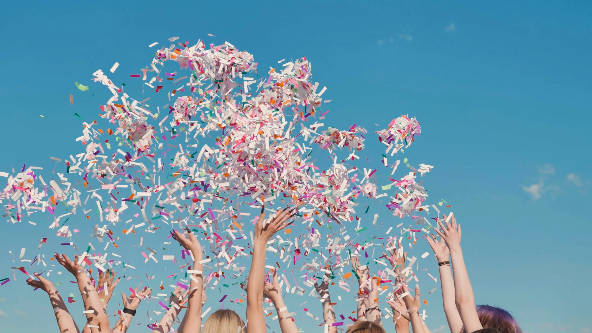 Group of students throwing colorful confetti in the air on a sunny day