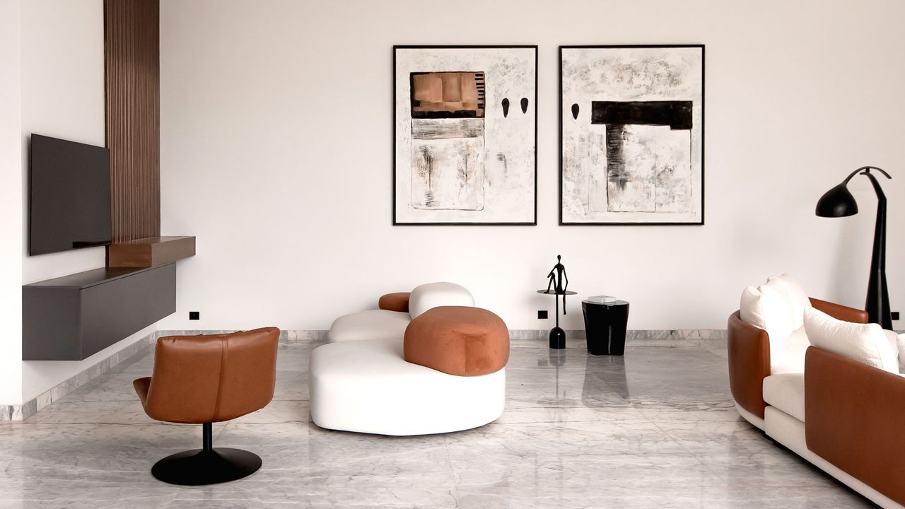 A living room with accent chairs and a white and brown sofa. Abstract art work hangs on the walls 