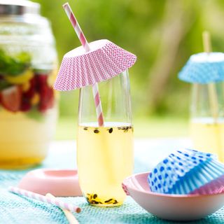 Fruit drink covered with cupcake case and straw on blue tablecloth