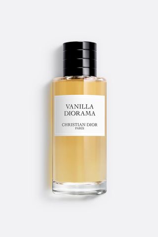 Dior Vanilla Diorama Eau de Parfum in tall circular light golden bottle with large white rectangular label and black ribbed cap on light grey background with shadow 