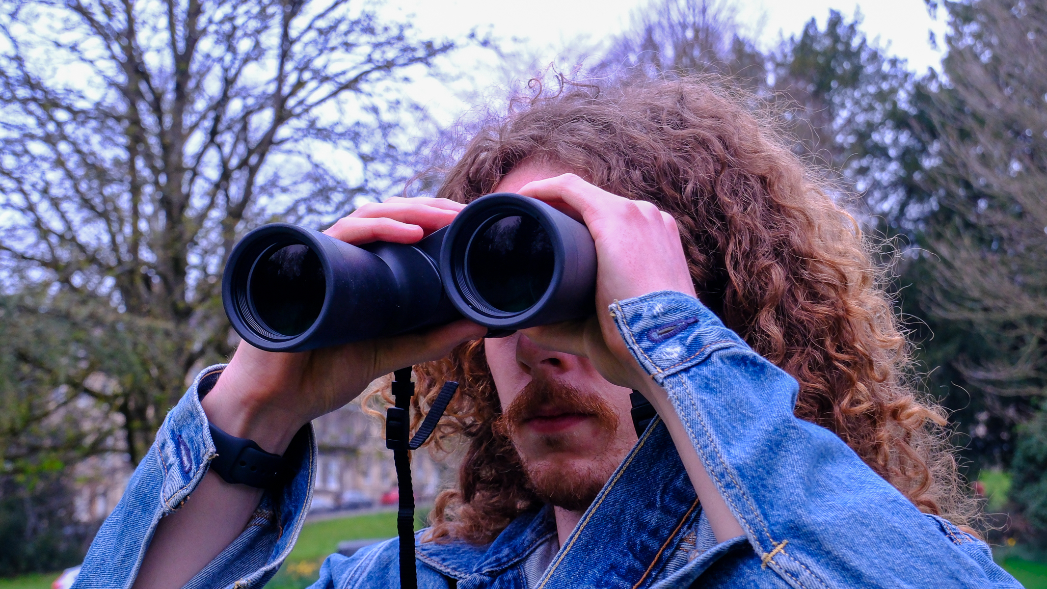 A man looking towards the sky, through the Nikon Action 7x50 binoculars, with trees in the background.