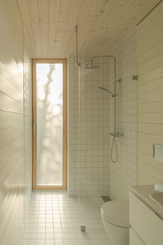 Bathroom with a slim vertical window. The shower is encased in white tiling