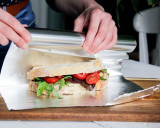 Person carefully wrapping tomato and lettuce white sandwich in aluminium foil