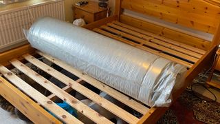 The Nectar Premier Hybrid mattress rolled up in its plastic wrapping on a bed