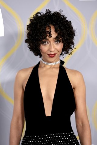 Ruth Negga with a curly bob and red lip.