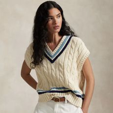 Woman wearing Ralph Lauren knit jumper and white jeans, against grey background