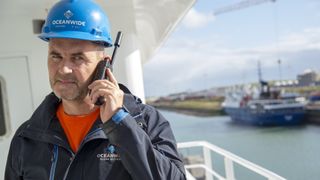 Man in hard hat using an Iridium Extreme satphone on a ship at sea