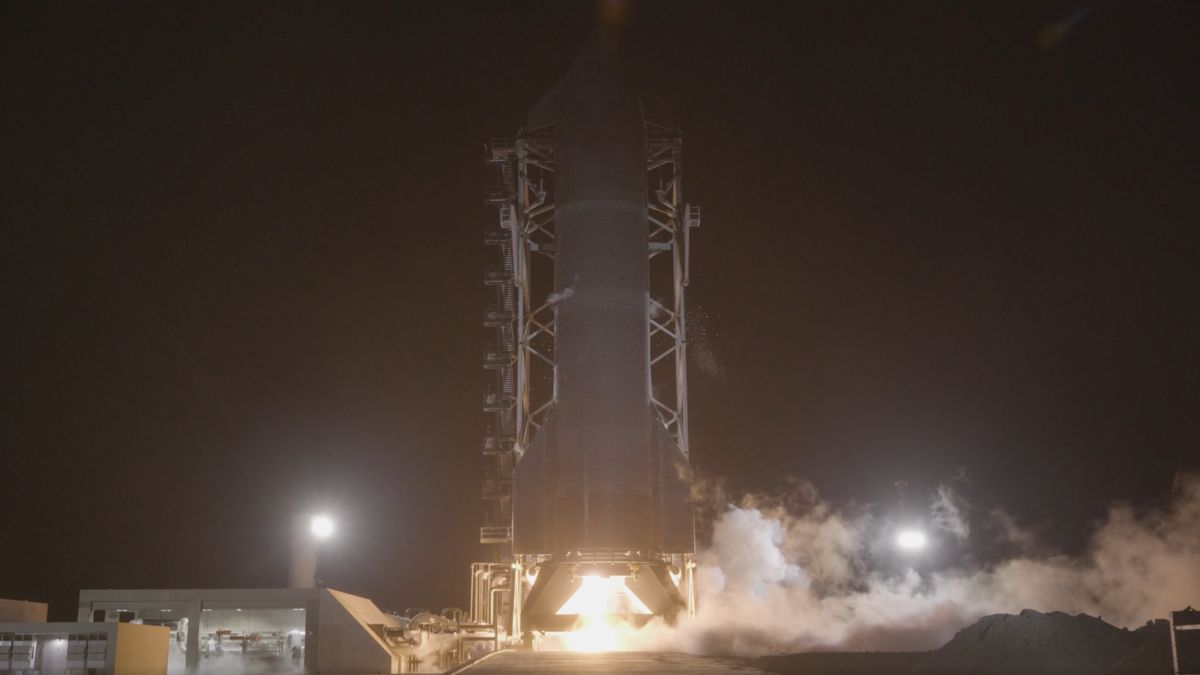 A tall finned black rocket fires an engine on a test stand in the black of night.