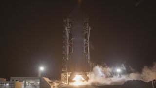 A tall finned black rocket fires an engine on a test stand in the black of night.