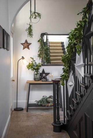 A Scandinavian-style black and light wood hallway decorated with green foliage on bannister and star decor